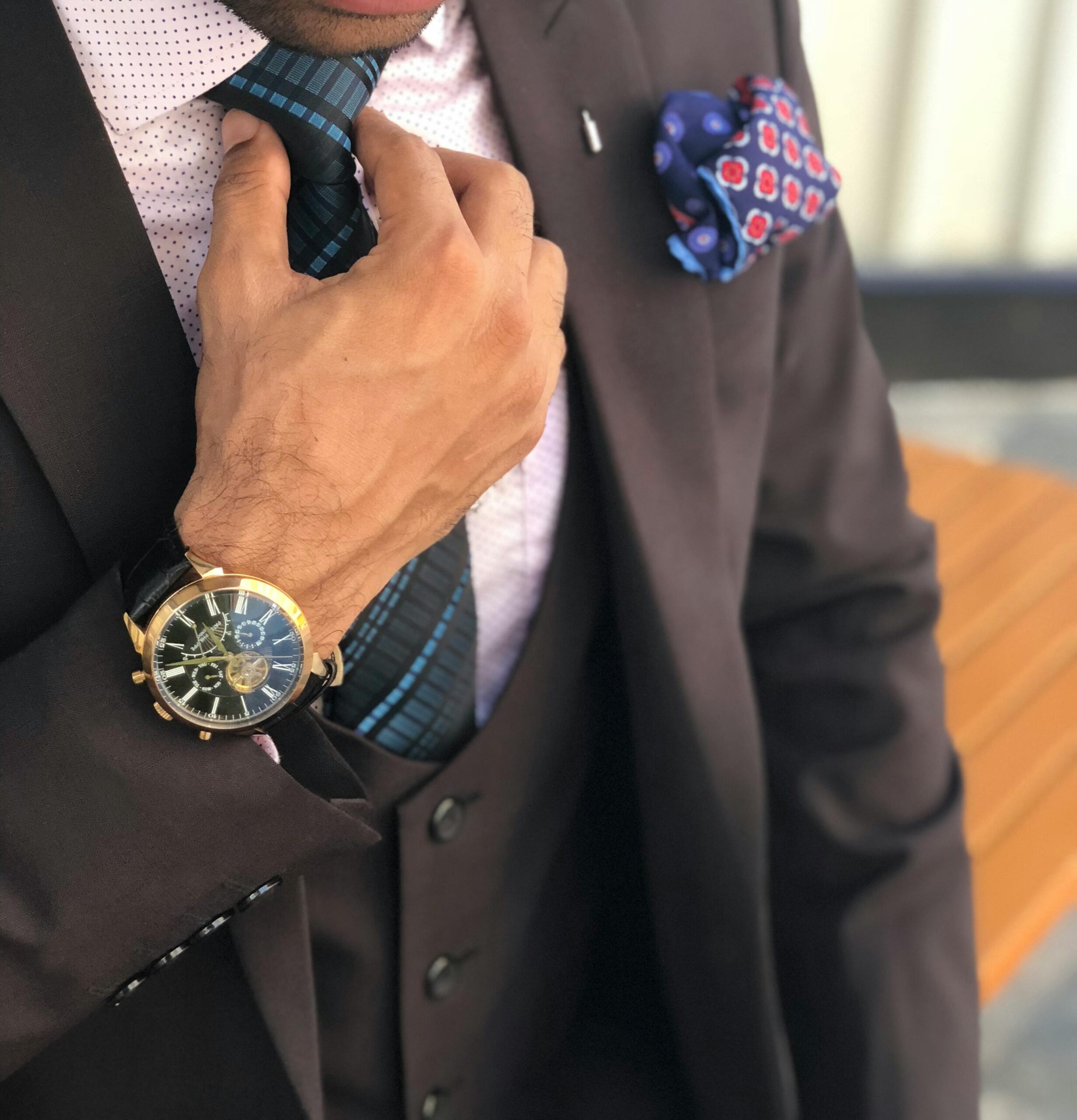 Elegant close-up of a man in a designer suit adjusting his tie, showcasing luxury fashion.