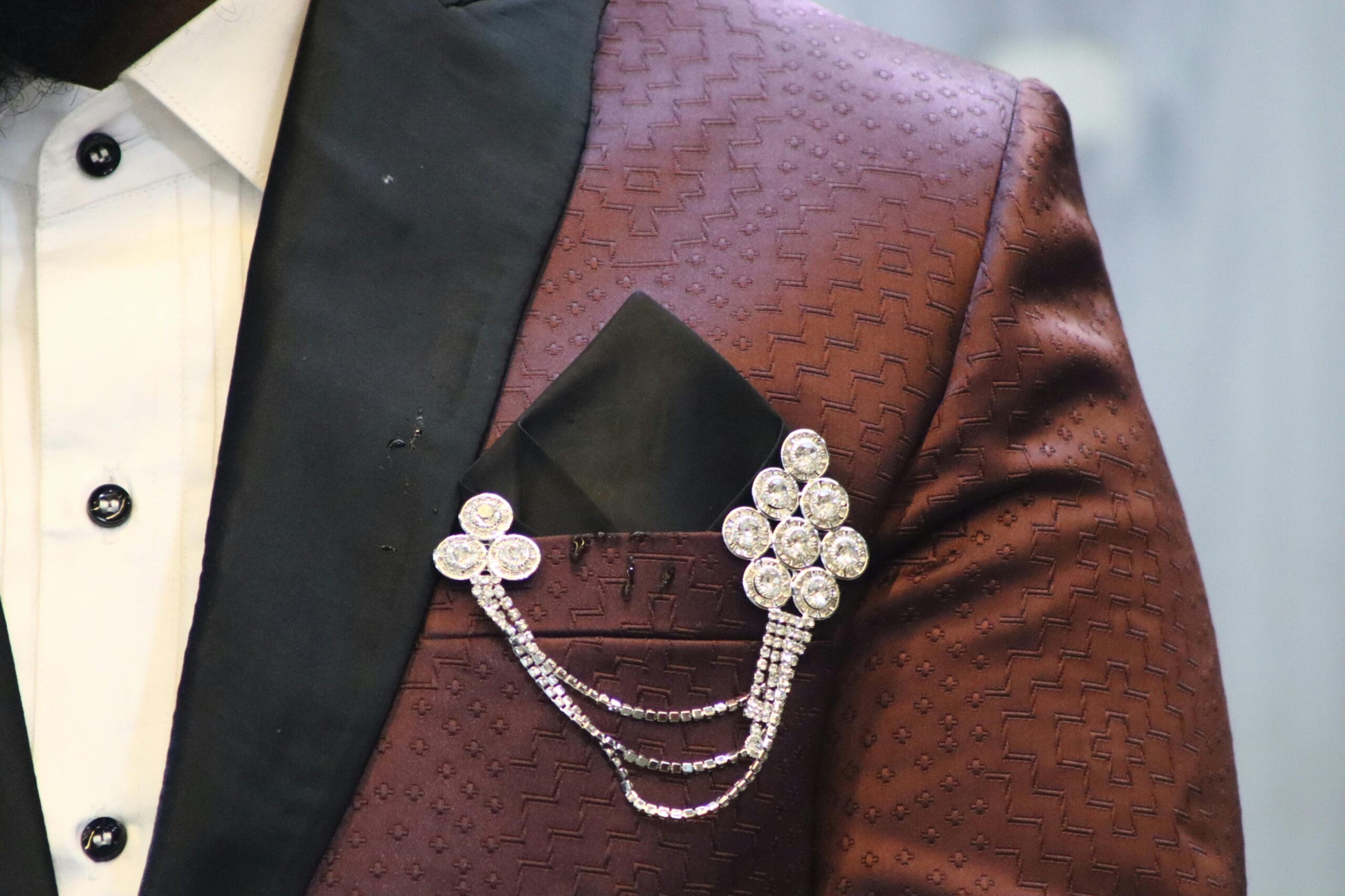 Close-up of a stylish brown brocade suit with a sparkling crystal brooch accent.